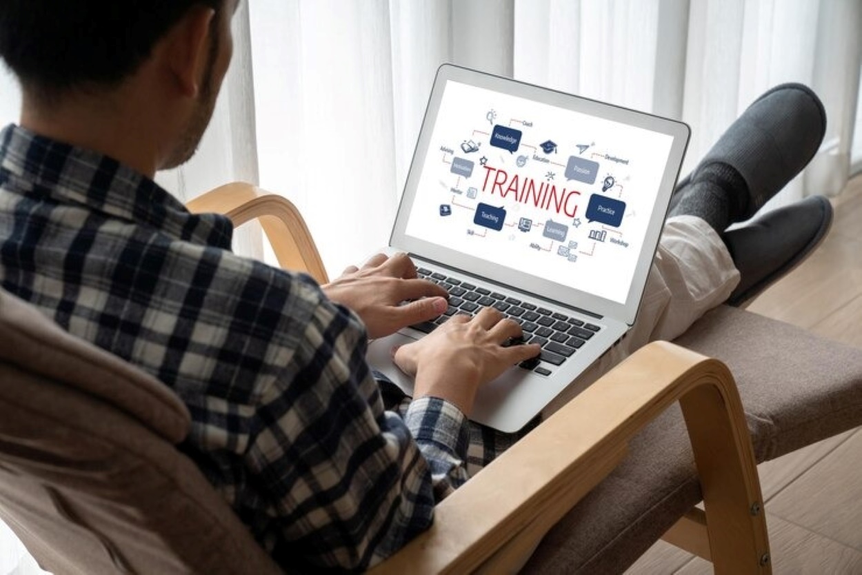 Employee Onboarding Software 3 | AD-IOS Web Development Person sitting in a chair typing on a laptop; the screen shows a training diagram with the word TRAINING in the center.